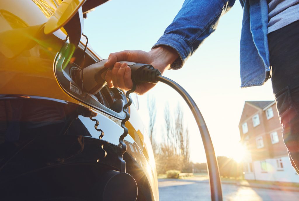 A man plugging in an electric car outside a home