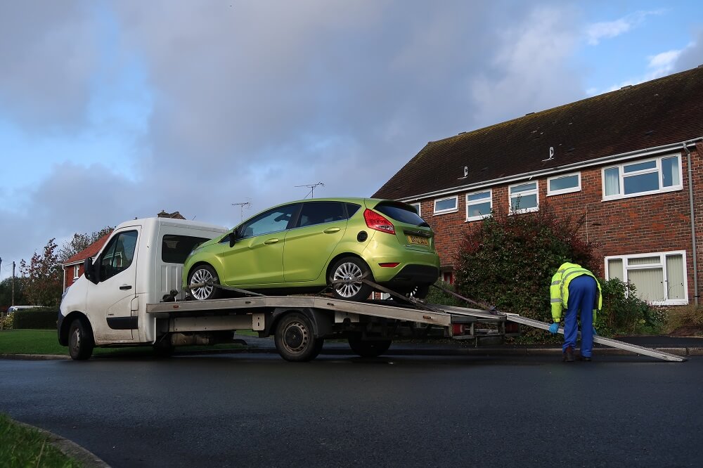 A green car being loaded onto the back of a flatbed truck